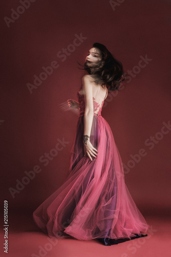 Beautiful girl model in a long red dress on a background of the color of the wine is spinning.