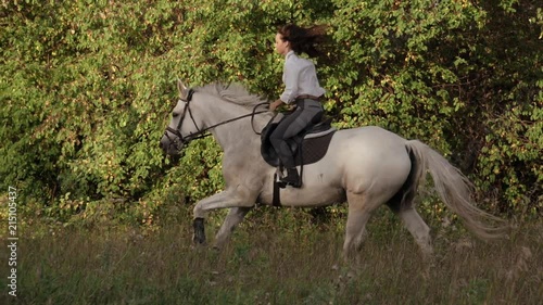A pretty girl jumps on her white horse at a gallop. Slow motion mode. photo