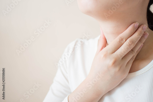 Sick women suffering from sore throat on gray background w/ copy space. Causes of throat pain include flu, common cold, bacterial infections, allergies, smoke, GERD or tumor. Close up. photo