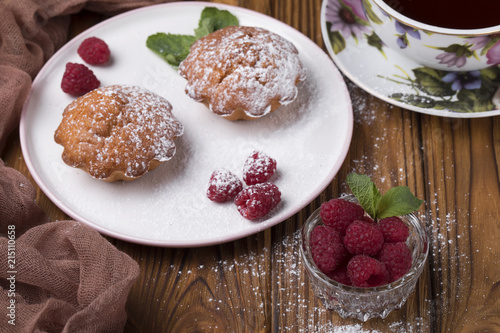 Capcake with raspberries and sugar powder on the table with tea teapot.