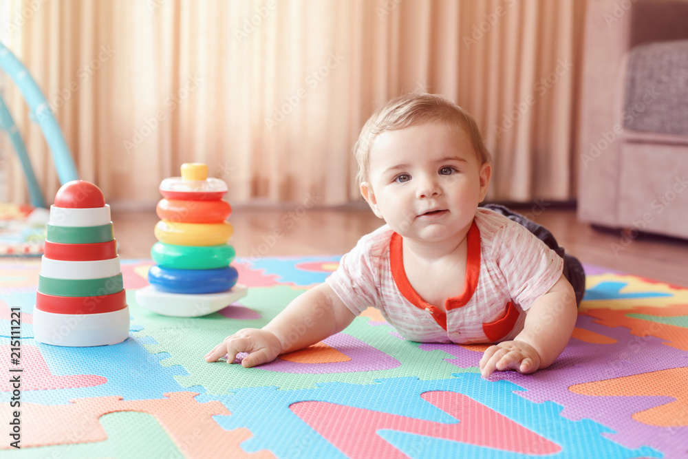 Portrait of cute adorable blond Caucasian smiling child boy with blue eyes crawling on floor in kids children room. Little baby playing with toys on playmat at home. Early education development Portrait of cute adorable blond Caucasian smiling child boy with blue eyes crawling on floor in kids children room. Little baby playing with toys on playmat at home. Early education development