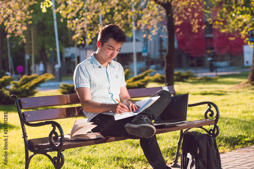 Student making the notes sitting on a bench in the park Student making the notes sitting on a bench in the park