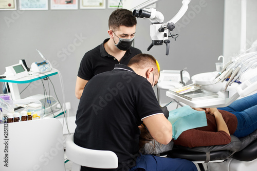 Assistant in a black mask and gloves helps the dentist in the process of treating the patient. Modern dentistry with the use of new technologies