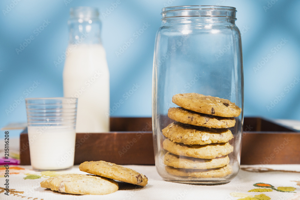 Composition with a cookie pile and milk bottle in a table. Morning sun in a blue background with texture. Composition with a cookie pile and milk bottle in a table. Morning sun in a blue background with texture.