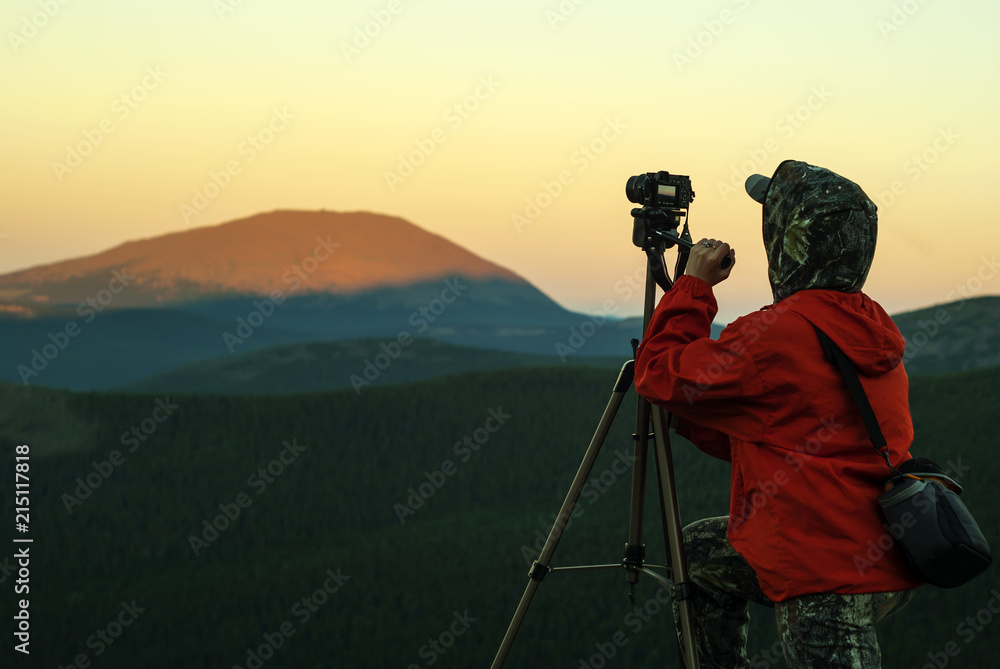 woman photographer takes a picture of a dawn in the mountains by camera on a tripod