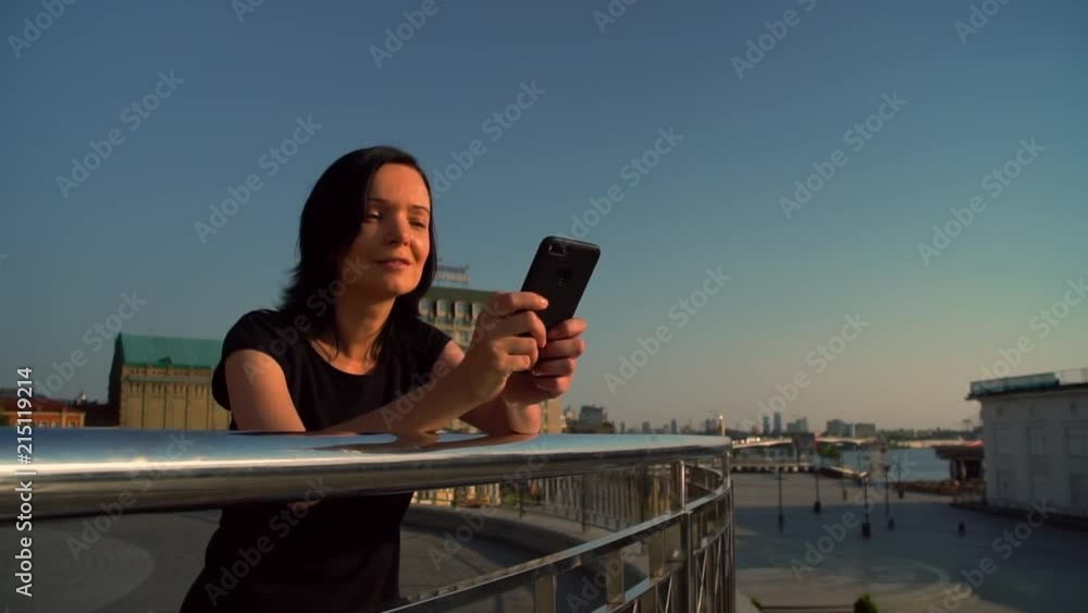 brunette woman using her mobile phone with city landscape background. elegant lady leaned against metallic enclosure. brunette woman using her mobile phone with city landscape background. elegant lady leaned against metallic enclosure.