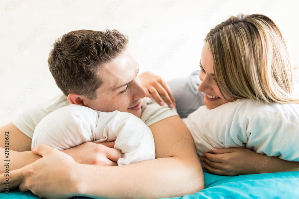 Couple Looking At Each Other While Embracing Pillows On Bed Couple Looking At Each Other While Embracing Pillows On Bed