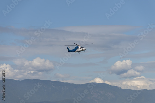 helicopter flies over the mountains covered with forest, under the clouds