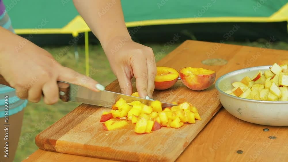 Young woman cuts a peach knife with a knife for fruit salad on a picnic. Young woman cuts a peach knife with a knife for fruit salad on a picnic.