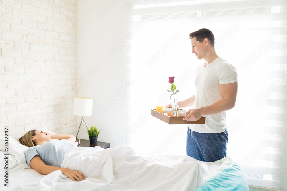 Male With Breakfast Tray Looking At Female Sleeping In Bed Male With Breakfast Tray Looking At Female Sleeping In Bed
