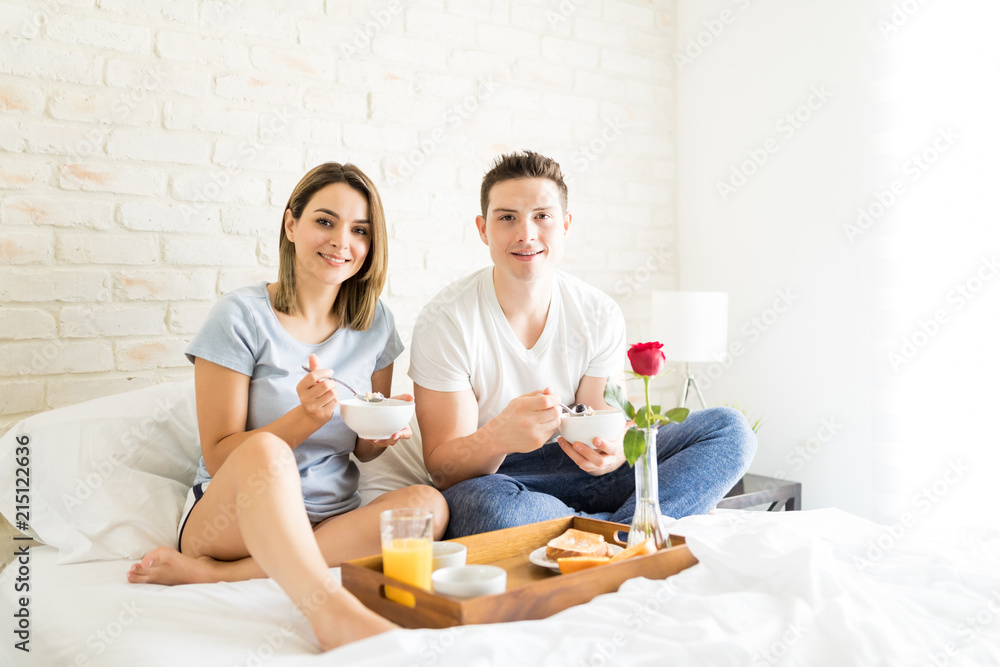 Smiling Couple Having Bowls Of Cereal In Bed Smiling Couple Having Bowls Of Cereal In Bed