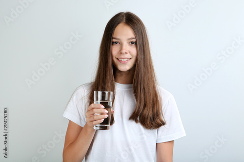 Beautiful young girl with glass of water on grey background