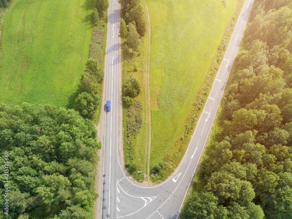Aerial view of highway with car. Aerial view of a country road with moving car. Car passing by. Aerial road. Aerial view flying. Captured from above with a drone. Soft lighting - obrazy, fototapety, plakaty 