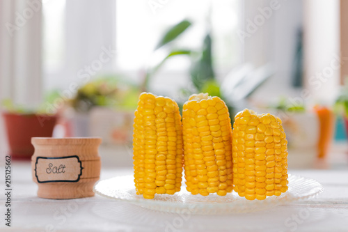 vertically built boiled corn next to a jar of salt on the background of the window photo