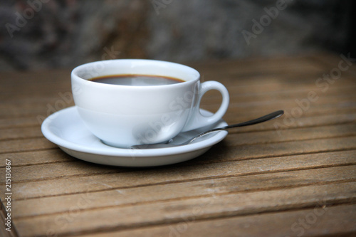 White cup with brown coffee on a wooden table.