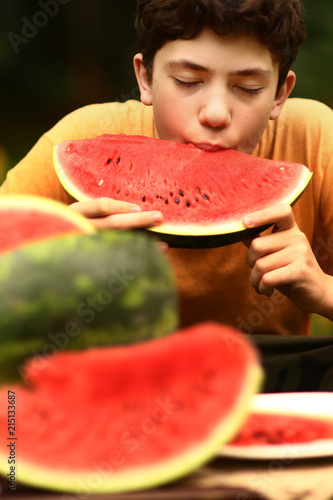 teenager boy eating cut water melon close up photo on green garden background photo