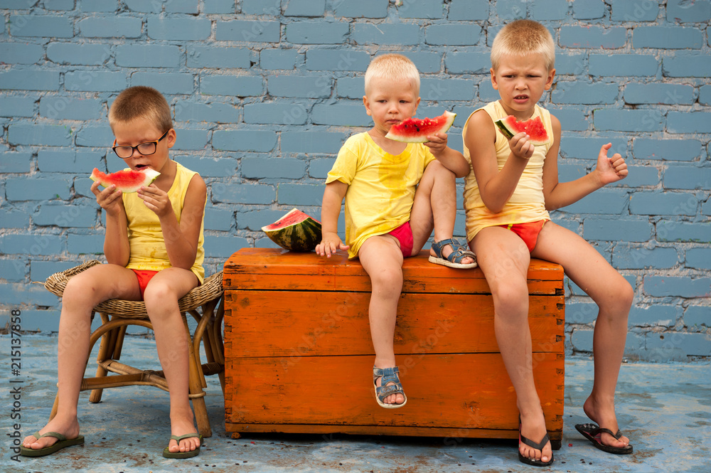 Funny village children eat watermelon sitting on old chest in courtyard of  village house. Boys brothers are happy together. School holidays in village.  Parents take care of kids. Eco-friendly products Stock Photo |