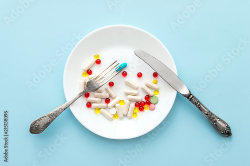 Many different weight loss pills and supplements as food on round white plate with fork and knife. diet pills and supplements, prescription weight loss drugs, appetite suppressants for dieting concept photo