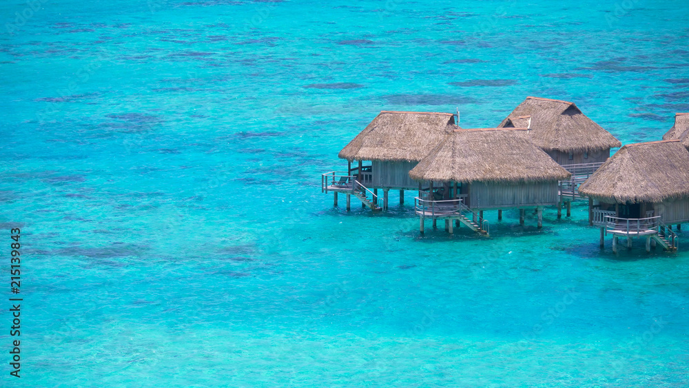 Tranquil turquoise ocean water surrounds the wooden bungalows on a sunny day.