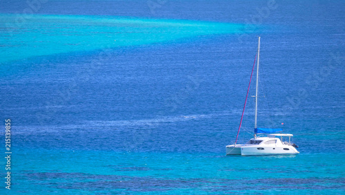 White sailboat resting in the tranquil turquoise ocean water on a sunny day.