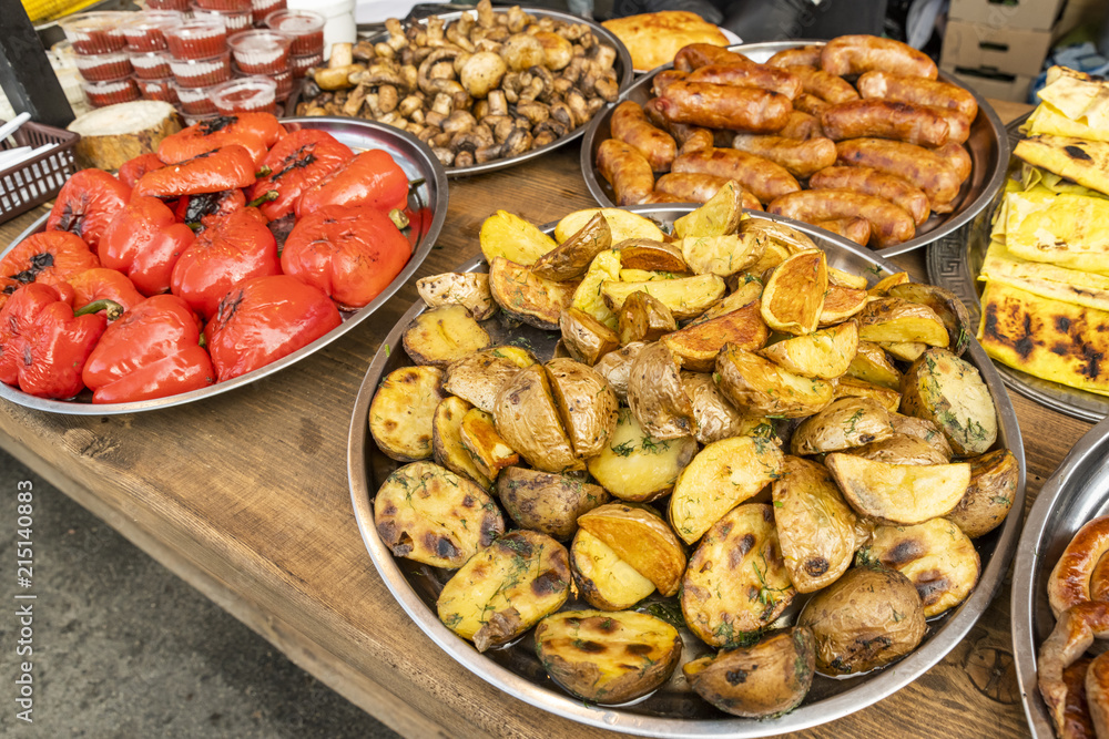 fried potatoes sliced in large slices laid out on a large metal plate, with fried sausage and baked vegetables and ketchup in plastic containers on a fast food table fried potatoes sliced in large slices laid out on a large metal plate, with fried sausage and baked vegetables and ketchup in plastic containers on a fast food table