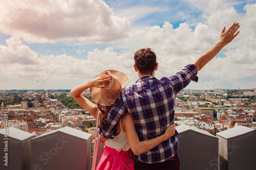 Young couple of tourists with raised hands looking on Lviv, Ukraine from viewpoint