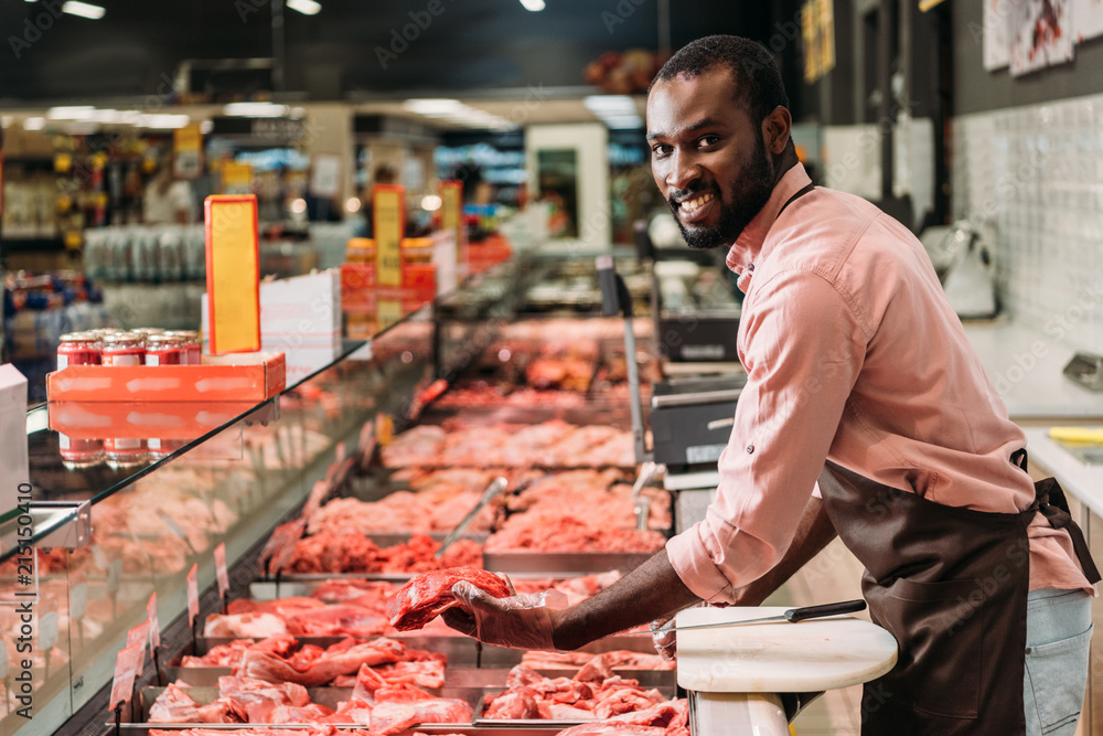 selective focus of african american male butcher in apron with steak of raw meat in grocery store selective focus of african american male butcher in apron with steak of raw meat in grocery store