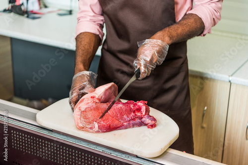 cropped image of african american male butcher in apron cutting raw meat in supermarket