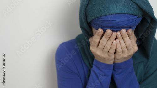 A Muslim woman wearing a hijab cries covering her face with her hands.