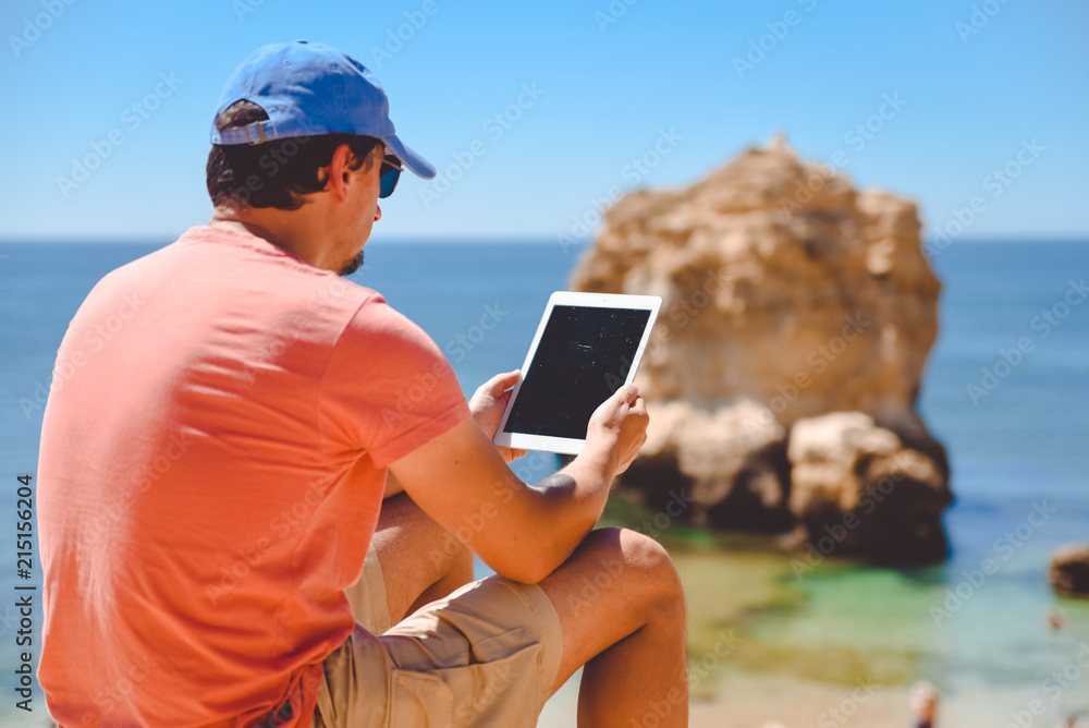 Back side view of person sitting holding tablet computer on ocean sunny natural background. Traveler having fun on international travelling lifestyle, technology social communication, amazing nature.