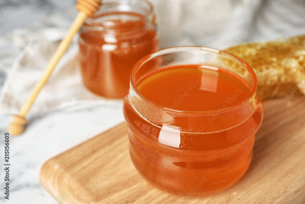 Glass jar with sweet honey on wooden board, closeup Glass jar with sweet honey on wooden board, closeup