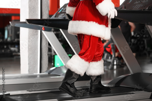 Authentic Santa Claus training on treadmill in modern gym, focus on legs