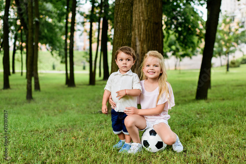 little brother and sister with football ball embracing in park