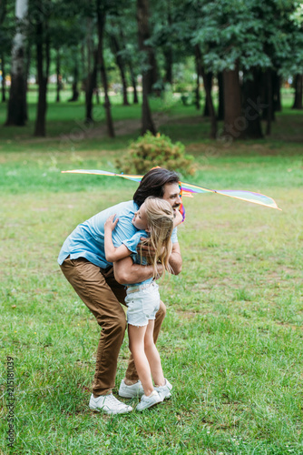 handsome happy father with kite embracing his little daughter at park