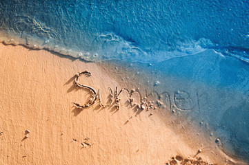 Summer passed the concept. The wave washes away the word summer written on the sand. End of vacation and season.