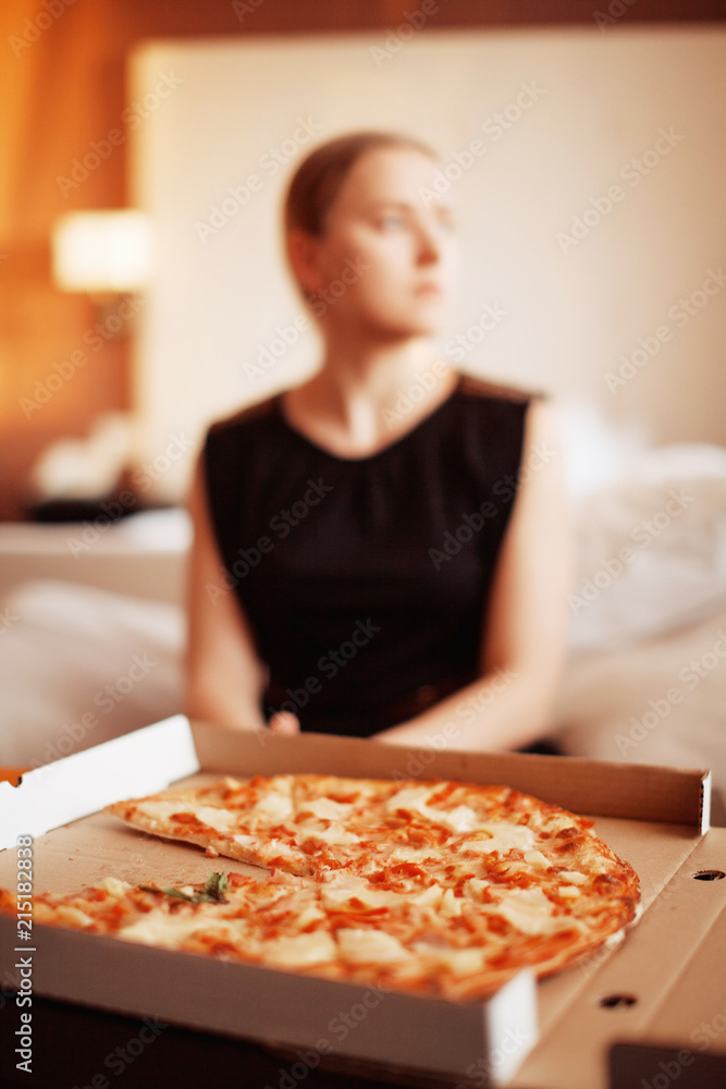 Beautiful blonde hungry woman sitting on sofa and eating hot tasty pizza alone. Junk food. Diet. Calories.