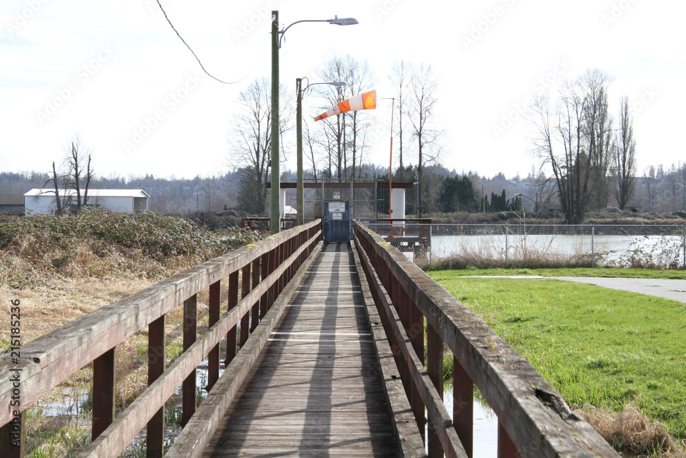 A wooden walkway leading to a gate and sign on the edge of the river.