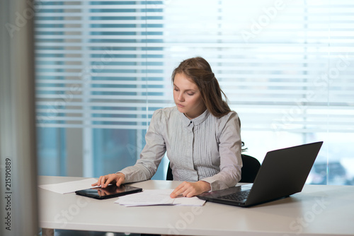 young girl businesswoman in casual clothes, sitting at a table closely look at documents, working at computer