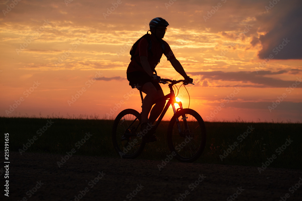Silhouette of a bicyclist traveling on a sunset background on the road to the field Silhouette of a bicyclist traveling on a sunset background on the road to the field