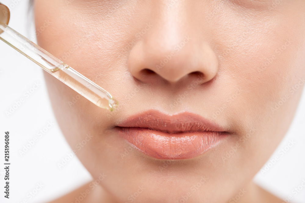 Close-up face of woman with pipette at lips on white background