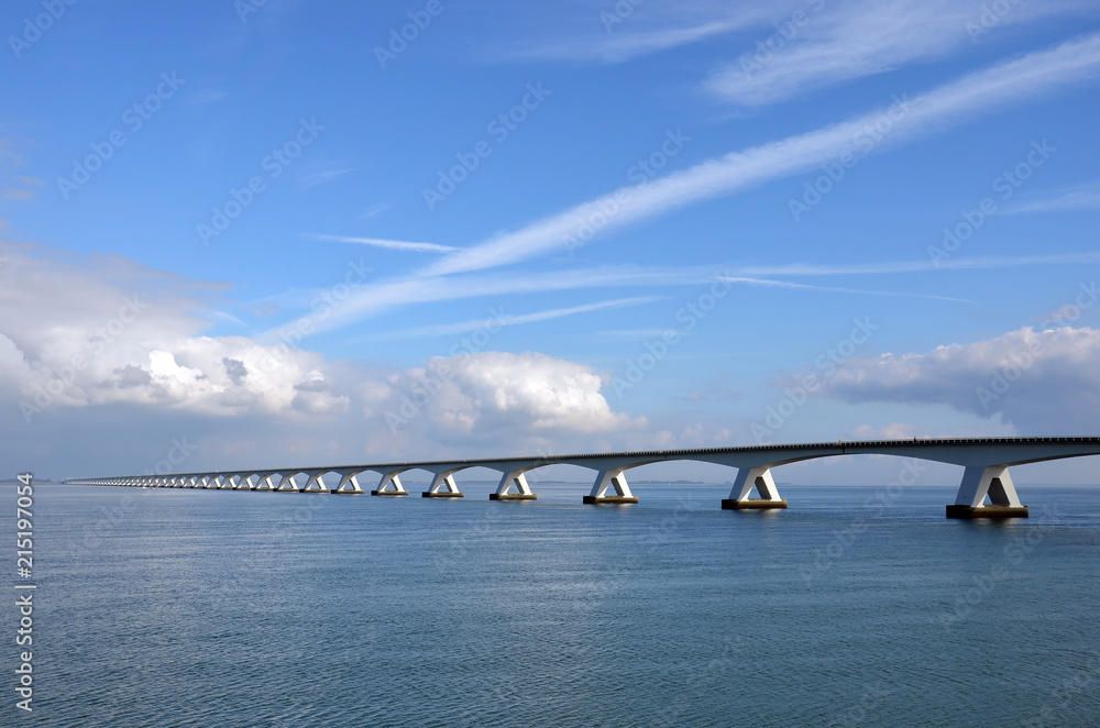 Obraz premium Zeeland Bridge and Oosterschelde estuary in the Netherlands, under a predominantly blue sky with some comulus clouds approaching