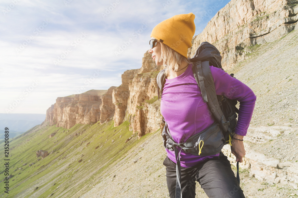 a tourist in sunglasses puts a backpack in the nature on the background of epic rocks preparing for trekking with climbing. The girl hiker fastens the fasteners on the backpack a tourist in sunglasses puts a backpack in the nature on the background of epic rocks preparing for trekking with climbing. The girl hiker fastens the fasteners on the backpack