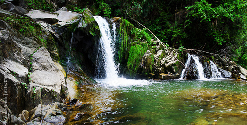 A stream in the mountains flows along the rocks and a stormy waterfall