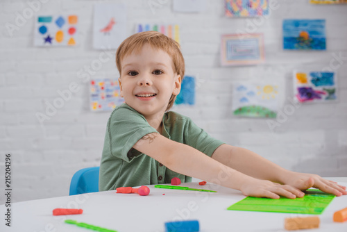 portrait of smiling boy sitting at table with colorful plasticine for sculpturing in room