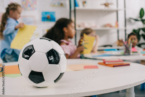 selective focus of soccer ball on table and multiracial preschoolers in classroom