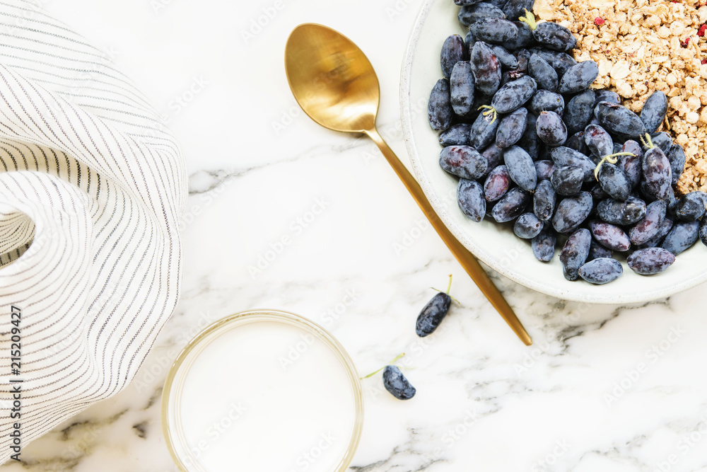 Fresh ripe honeysuckle berries and muesli in a ceramic bowl and cup of milk on a grey marble table. Healthy breakfast Fresh ripe honeysuckle berries and muesli in a ceramic bowl and cup of milk on a grey marble table. Healthy breakfast