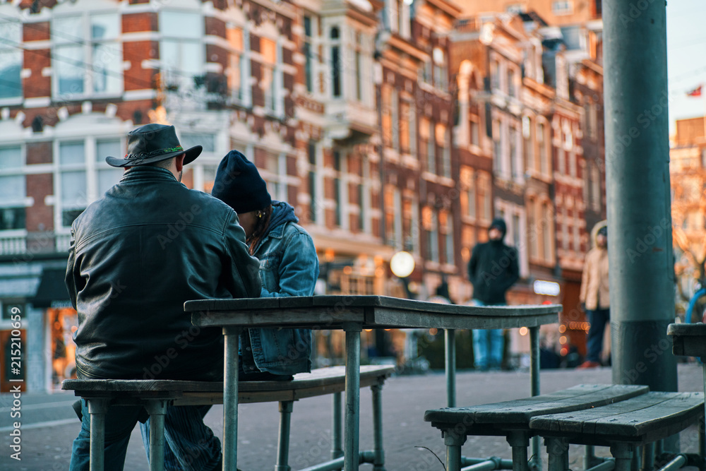 Man with hat and woman sitting on a bench in Amsterdam, afternoon, winter Man with hat and woman sitting on a bench in Amsterdam, afternoon, winter