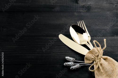 Fotografia, Obraz a set of bronze cutlery, spoon, fork and knife in a sack on black wooden table