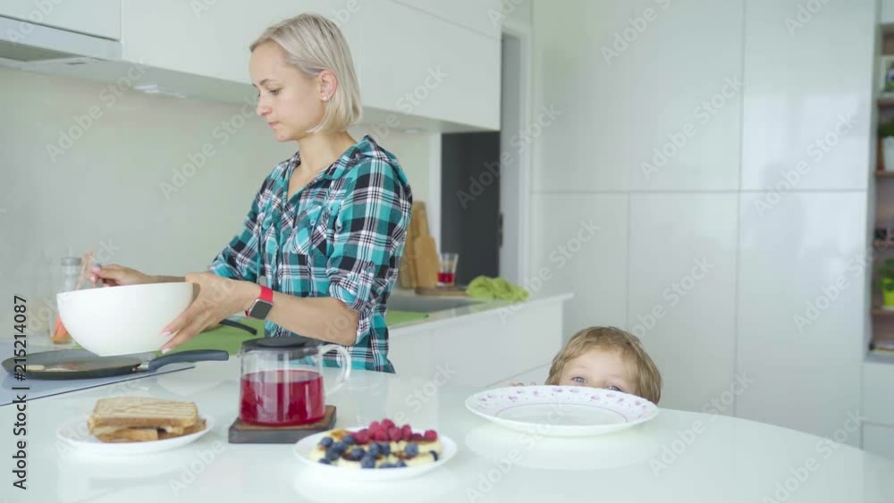 Mother cooking pancakes. Boy is stealing pancakes from plate. Mother cooking pancakes. Boy is stealing pancakes from plate.