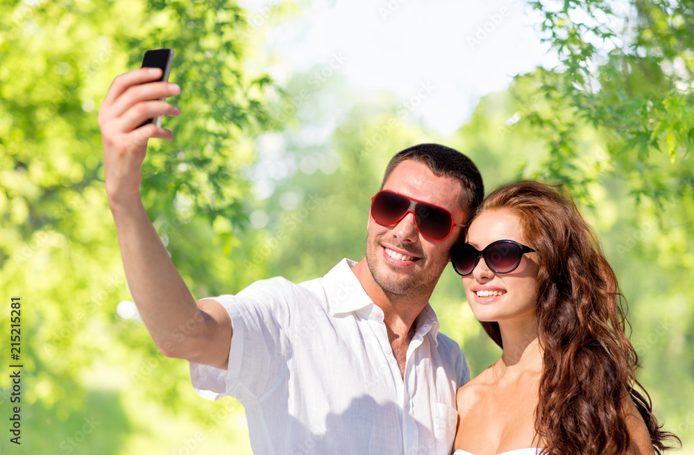 love, summer and technology concept - smiling couple in sunglasses making selfie by smartphone over green natural background